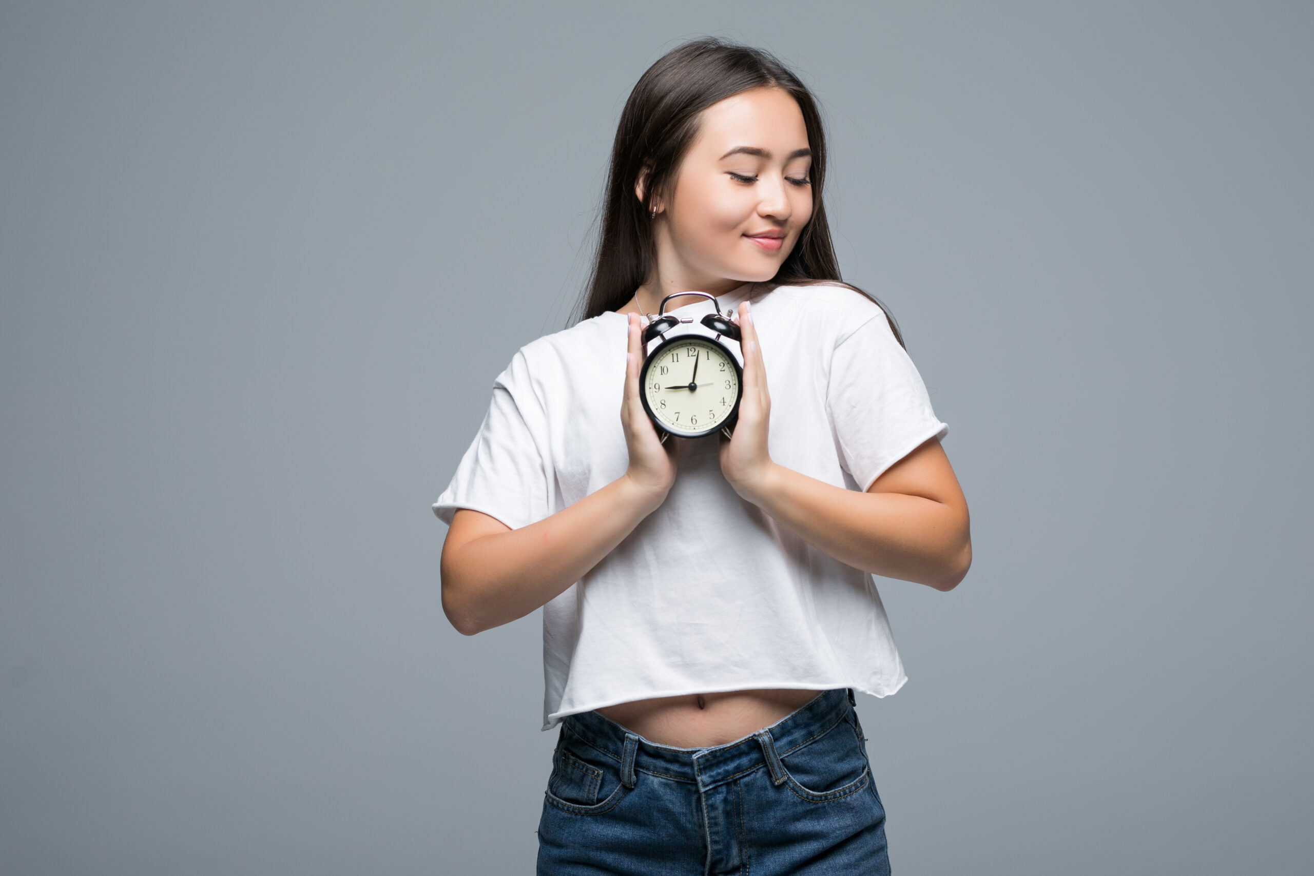 Young Asian woman smile with a clock on gray background