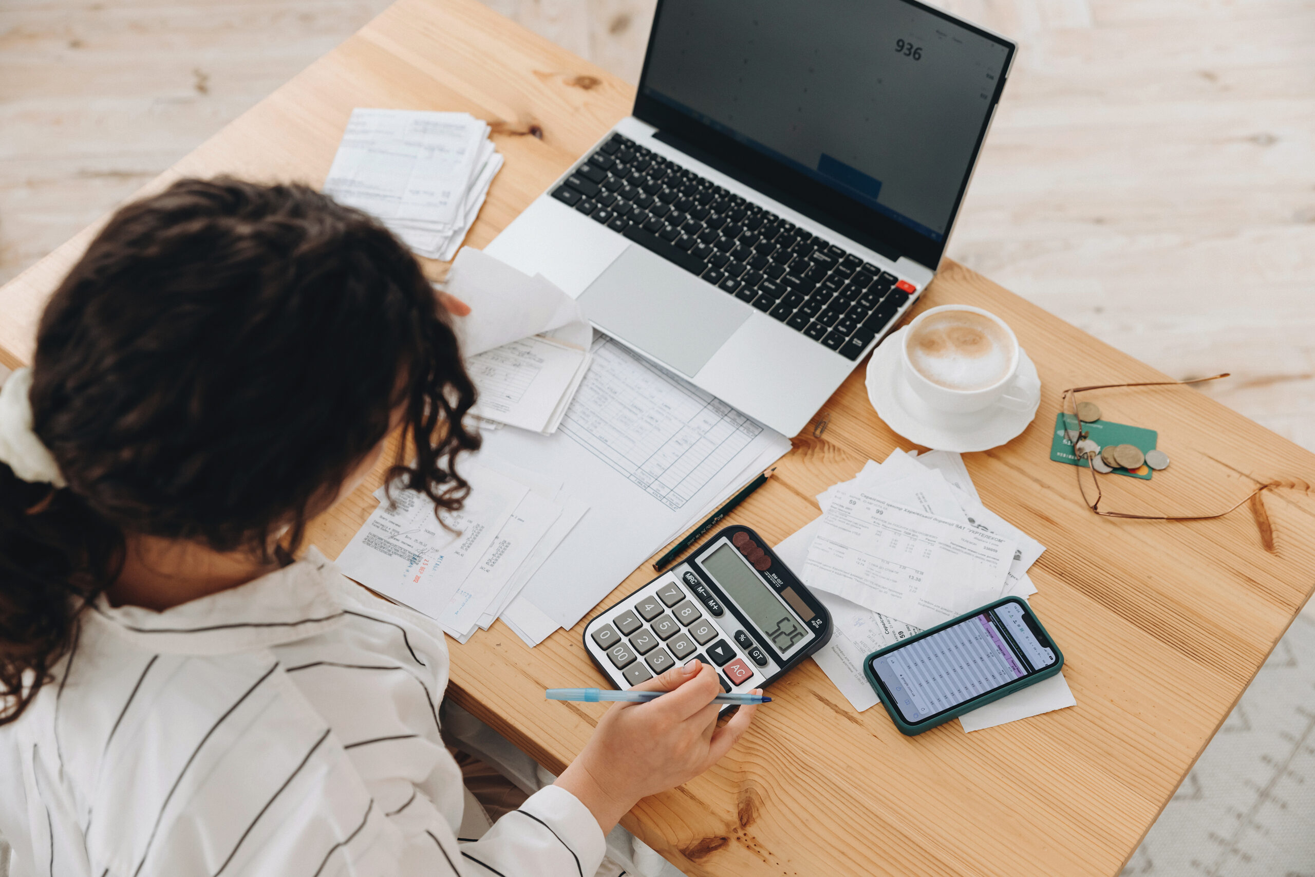 Top view of a woman working at home in the kitchen with financial papers, counting on a calculator, paying bills, planning a budget to save some money. Independent accounting, remote accountant.